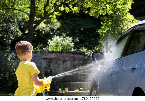 Little boy\
washing blue car in the summer garden.\
