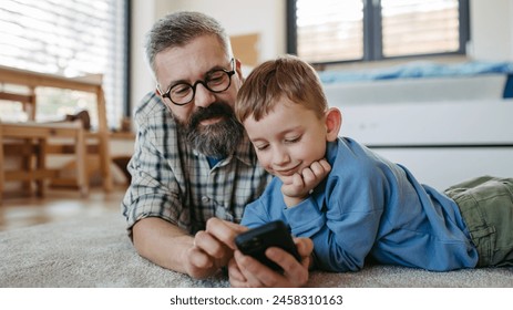 Little boy watching cartoon movie on smartphone with father, lying on floor in kids room. Dad explaining technology to son, digital literacy for kids. - Powered by Shutterstock