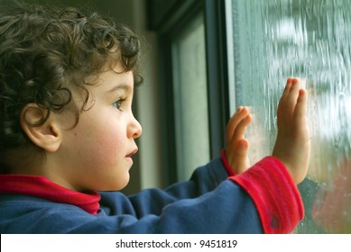 little boy watching the rain through the window
