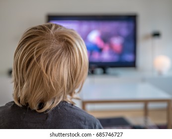 A Little boy watching TV at home. View from behind sofa. Blond hair.