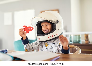 Little Boy Wearing An Astronaut Helmet Costume And Playing With A Spaceship While Doing Homework. Cute Kid In Astronaut Pajamas With Toy Rocket Playing And Dreaming Of Becoming A Spacemen.