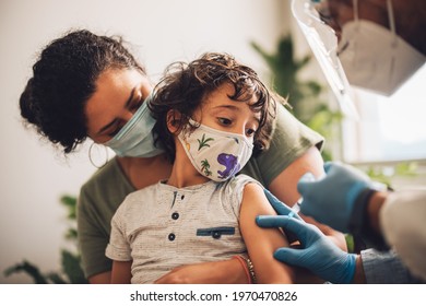 Little Boy Wearing Face Mask Taking Vaccine At Home. Kid With Mother Receiving Covid Vaccine From A Healthcare Worker At Home.