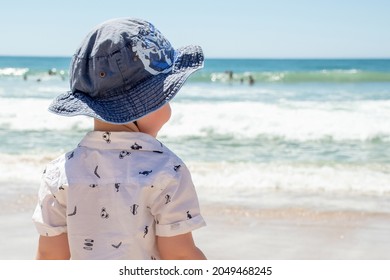 Little boy wearing hat on a sandy ocean beach in Australia. Sun safety - Sunscreen, hat and shirt. Travel with kids - Shutterstock ID 2049468245