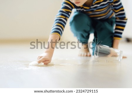 Little boy wipes water spilled from a glass on the floor. Teaching a child to clean up after himself. Responsibility, accuracy. Help around the house. Household duties. Housework.