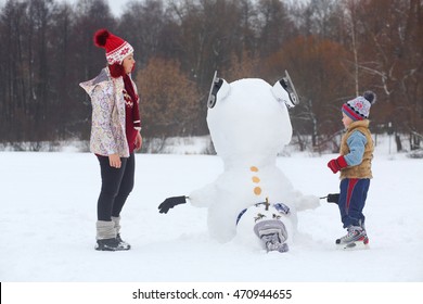 Little boy and woman stand near upside down snowman at winter day