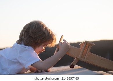 Little Boy With Wooden Plane, Boy Wants To Become Pilot And Astronaut. Happy Child Play With Toy Airplane. Kids Pilot Dreams Of Flying. Childhood Dream Imagination Concept.