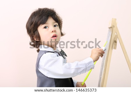 Little boy with yellow pointer draws with chalk on chalkboard in studio.