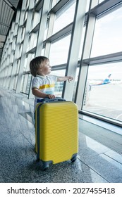 Little Boy With Yellow Suitcase At Empty Airport Terminal. Kid In T-shirt And Shorts Stands At Lounge Waiting For Plane Flight. Family Trip And Vacation Concept.