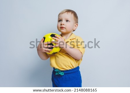 A little boy in a yellow t-shirt with a soccer ball in his hand smiles isolated on a white background. Sports child holding a ball. Children's sports game. Little athlete.