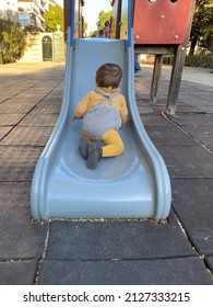 Little Boy In Yellow Vest Playing, Trying To Climb Up A Slide At