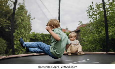 Little boys, brothers jumping on trampoline in the backyard, doing somersaults. Dangers and risks of trampoline for kids. - Powered by Shutterstock