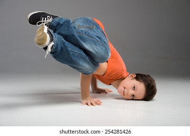 little break dancer showing his skills on grey background. Hip hop dancer boy performing isolated over dark background 