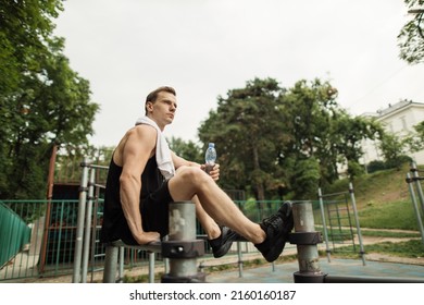 Little Break. Young Athletic Guy With Muscular Body, Sportsman And Fitness Model, Strong Man Sitting On Parallel Bars. Athletic Body Shape, Guy Relax At Outdoor Gym.