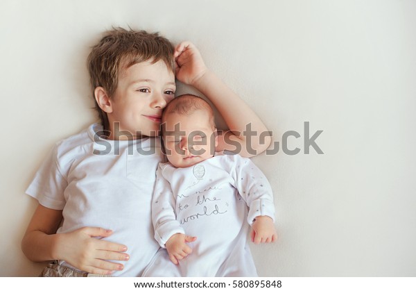 Little\
brother hugging her newborn baby. Toddler kid meeting new sibling.\
Cute boy and new born baby girl relax in a white bedroom. Family\
with children at home. Love, trust and\
tenderness