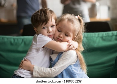 Little brother hugging upset sister sitting together on couch at home, sincere toddler boy embracing depressed girl, apologizing, supporting, good relationship, friendship, compassion, empathy concept