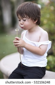 Little Brown Haired Boy In A White Wife Beater T-shirt Blowing A Dandelion