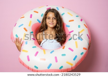 Little brunette cute girl holding a big rubber ring on pink background. Active holidays with family on the beach pool. Emotional kid