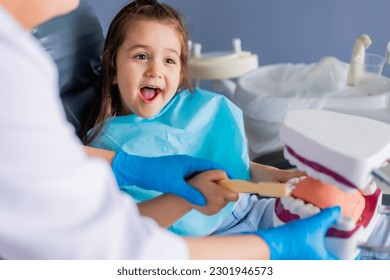 little brunette girl at a dentist's appointment studies a mannequin with a doctor, learns to brush her teeth. Pediatric dentistry - Powered by Shutterstock