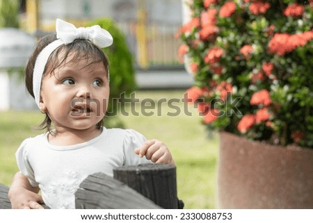 Little brunette girl with a look of surprise and disgust, looking upwards, standing next to a black wooden fence
