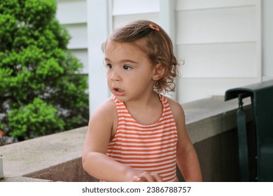 Little brunette toddler girl, upclose portrait on porch with stone wall behind her. 