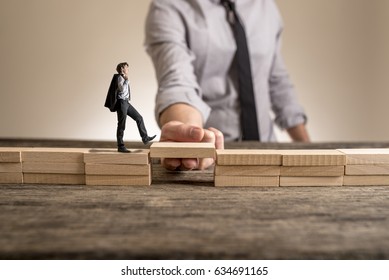 Little businessman walking across bridge, while the hand of other man holding it for him.