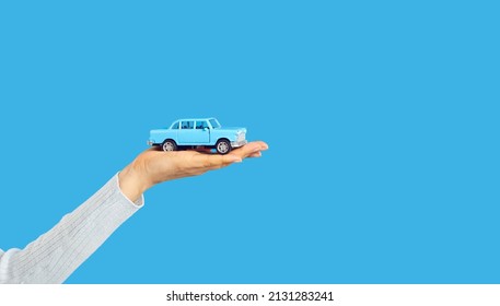 Little Car On Open Woman's Hand On Blue Text Copyspace Studio Background, Cropped Shot. Salesperson Or Driver Holding Little Auto. Adult Person Playing With Toy Car. Insurance, Rent, Lending Concept