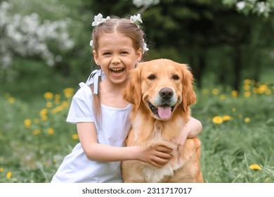 a little caucasian beautiful girl in denim shorts and a white t-shirt sits and hugs a dog golden retriever labrador in flowering gardens in the park. The dog is man's best friend. - Powered by Shutterstock