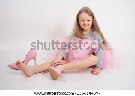a little caucasian blonde girl sits and puts on her mother's high-heeled shoes. kid wanna to be fashionable and in style.
