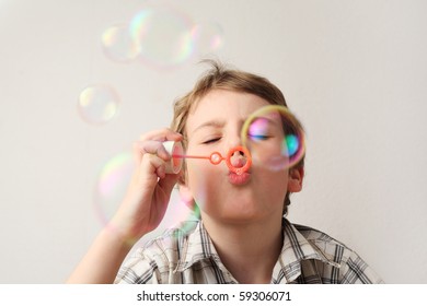 little caucasian boy blowing soap bubbles on white background, front view