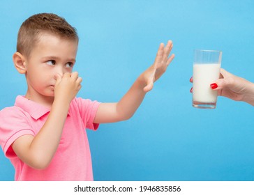 Little Caucasian Boy Clamps His Nose With His Hand And Refuses To Drink Milk, Yogurt. Mother's Hand With A Glass Of Yogurt Or Milk. Lactose Intolerance. Dairy Intolerant Child Refuses To Drink Milk