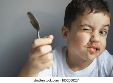 Little caucasian boy eating chocolate. Grey background. Cute happy kid covered by chocolate. Childhood concept