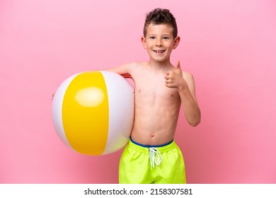 Little caucasian boy holding a beach ball isolated on pink background with thumbs up because something good has happened