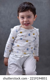 Little Caucasian boy in pajamas smiling sitting in chair against a gray wall - Shutterstock ID 2219194851