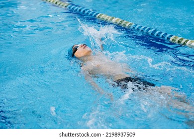 little caucasian boy wearing goggles swimming backstroke style in a pool. Image with selective focus - Powered by Shutterstock