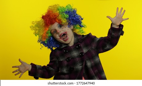 Little caucasian child girl clown in rainbow wig making silly faces. Five years old female kid having fun, smiling, dancing, looking at camera. Expressions. Copy space. Halloween. Yellow background