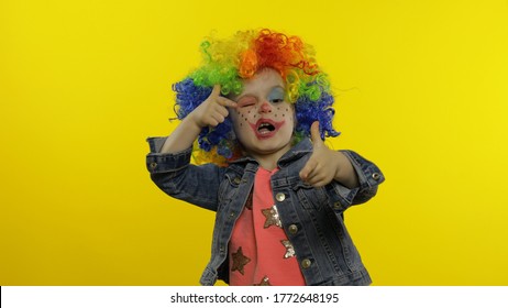 Little caucasian child girl in clown cosplay making silly faces. Colorful wig. Happy five years old female kid having fun, smiling, dancing, looking at camera. Halloween. Isolated on yellow background