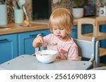 Little Caucasian child toddler girl eats chocolate balls with milk in the kitchen.