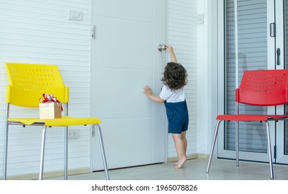 Little caucasian cute girl with curly hair wearing white shirt and blue overalls, playing and trying to open door in living room at home. Education concept - Powered by Shutterstock