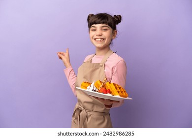 Little caucasian girl holding waffles isolated on purple background pointing back - Powered by Shutterstock