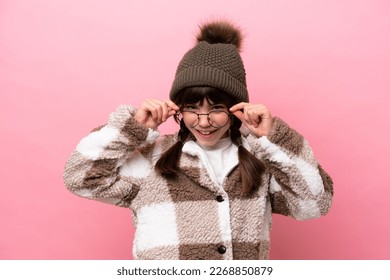 Little caucasian girl with winter jacket isolated on pink background with glasses and surprised - Powered by Shutterstock