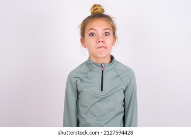 little caucasian kid girl with hair bun wearing technical shirt over white background making grimace and crazy face, screaming out of control, funny lunatic expressing freedom and wild.