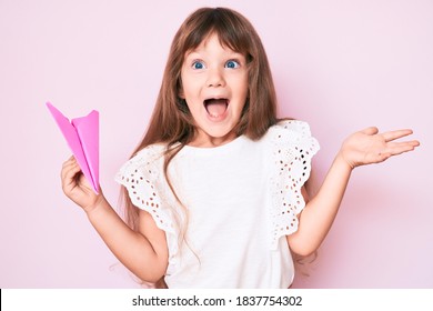Little caucasian kid girl with long hair holding paper airplane celebrating achievement with happy smile and winner expression with raised hand  - Shutterstock ID 1837754302