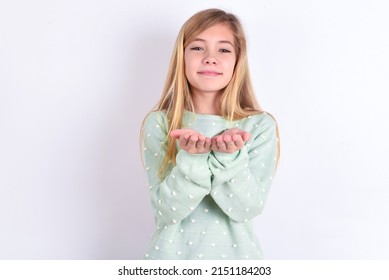 Little Caucasian Kid Girl Wearing Trendy Sweater Over White Background  Holding Something With Open Palms, Offering To The Camera.