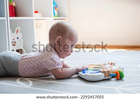 Little caucasian newborn baby girl playing with a piano toy on the floor during tummy time. Tummy time concept. Baby development. 