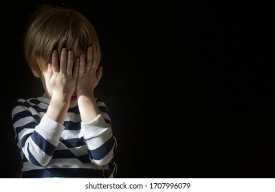 Little Caucasians blond boy child 3-4 years old covered his face with his hands alone in the dark and is afraid. The concept of social problems and dysfunctional families, child abuse. Copy space