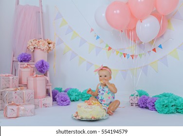 Little Charming Girl Celebrate Her First Birthday With Sweet Cake On A Light Party Background With Pink Gift Boxes, Flowers, Colorful Decorations, Garland And Balloons. Kids Party Organization