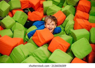 Little Cheerful Boy Enjoys Relaxing In Dry Pool Of Soft Cubes. Children's Entertainment In Play Center.