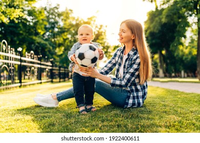 Little Cheerful Child With Mom Playing With Soccer Ball On The Lawn In The Park