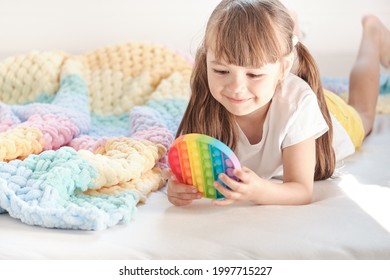 little cheerful girl plays in a multi-colored plastic toy pop it while lying on the bed. playing at home during summer holidays