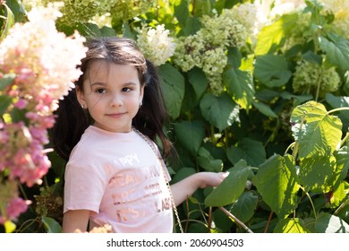 Little cheerful preschooler girl in the bushes of flowers